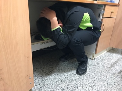 地震開始時，同學掌握蹲低、掩護及穩住要領，迅速躲至書桌下。(1)